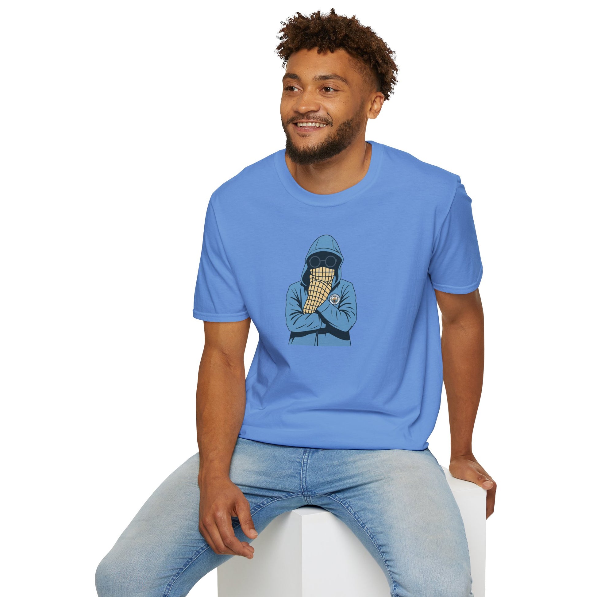 Smiling man wearing light blue t-shirt with hooded figure and ice cream cone design, sitting on white cube