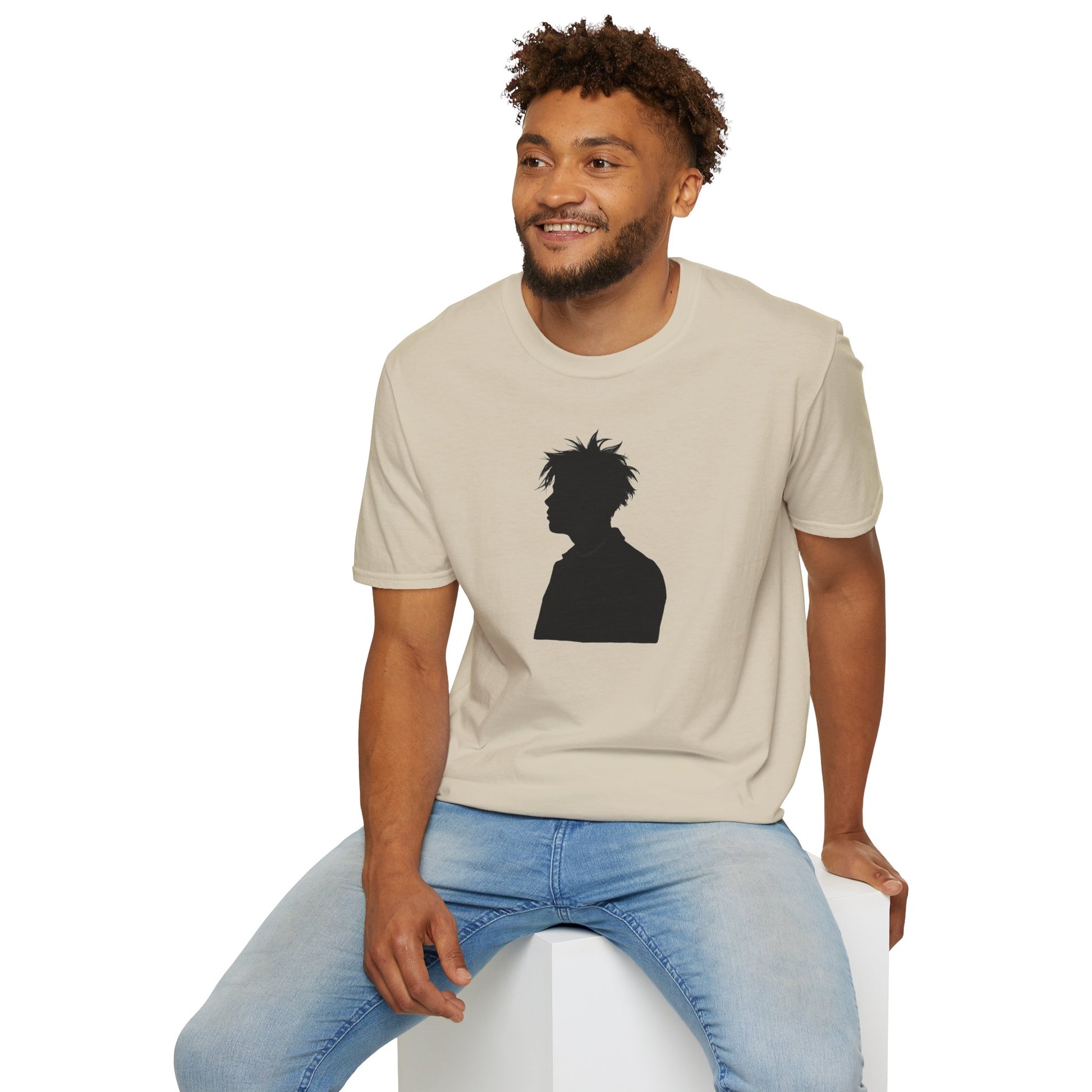 Smiling man wearing beige t-shirt with black silhouette graphic, sitting on white cube, casual jeans
