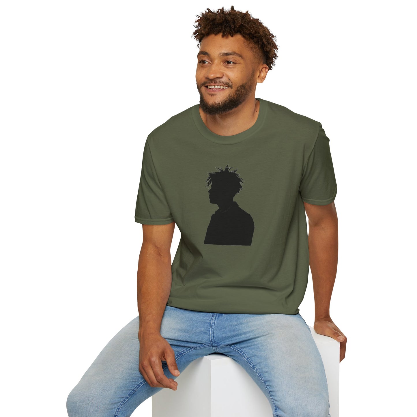 Man wearing olive green t-shirt with black silhouette graphic and light blue jeans sitting on white cube