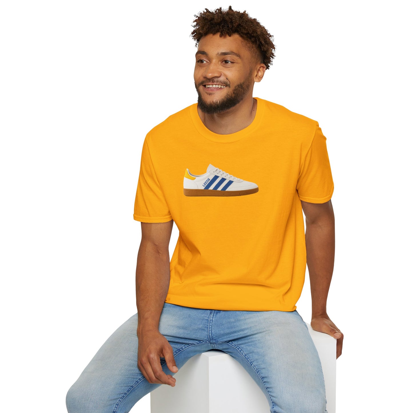 Smiling man wearing bright yellow t-shirt with blue and white sneaker graphic sitting on white cube