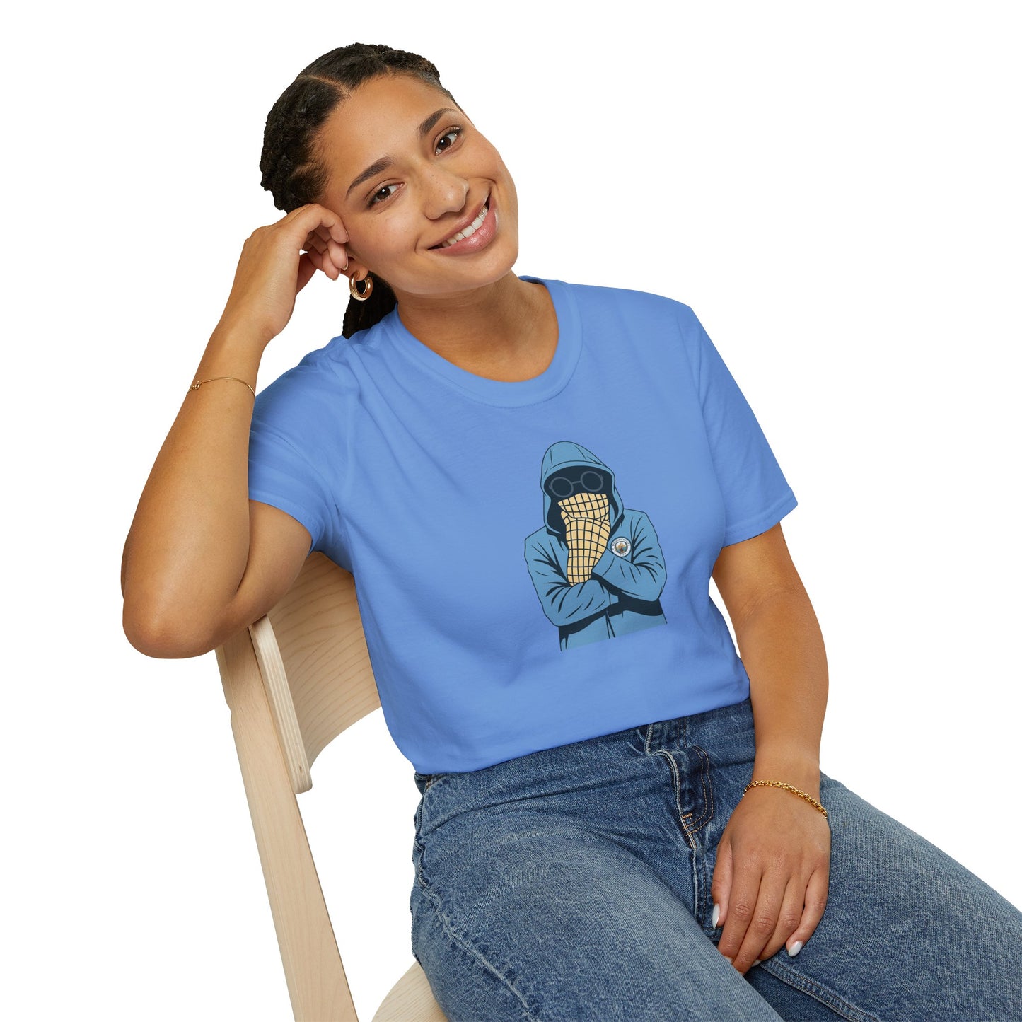 Smiling woman wearing light blue graphic t-shirt with hooded figure and sunglasses design, sitting on wooden chair